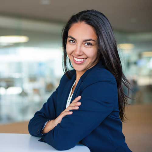 Hermosa y joven abogada sonriendo, sentada de brazos cruzados en las oficinas de Jinete y Asociados